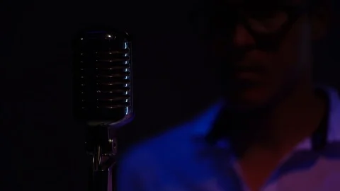 Man in a white regulate and fix the retro glare microphone. Spotlights shine. Video stock 118528847