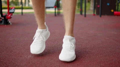 Man in white running sneakers doing light warm up jumps on an outdoor sport.. Video stock 341457626