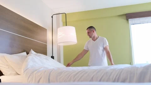 A man in a white shirt is making a bed in a hotel room Vídeo Stock 306041503