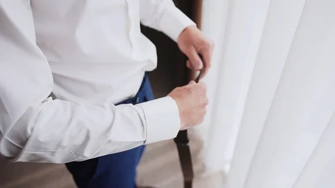 A man in a white shirt puts on a brown leather belt Stock Footage 129463520