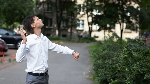 Man in white shirt stand under windows of house with phone, he sings and dance. Stock Footage 88041478