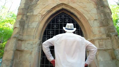 A man in a white straw hat approaches the archway of an old Gothic building. He Stock Footage 245482541