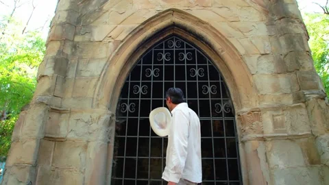 A man in a white straw hat walks in front of an old Gothic building. He takes Stock Footage 245481925