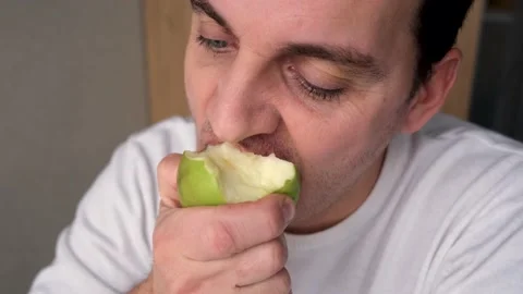 A man in a white sweater bites an apple looks pensively into the distance Stock Footage 168572638
