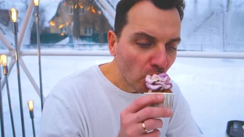 A man in a white sweater sits in the cafe and eats cupcake Stock Footage 169964480