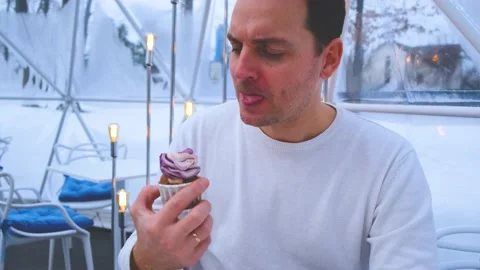 A man in a white sweater sits in the cafe tent sphere and eats a blueberry Stock Footage 169964756