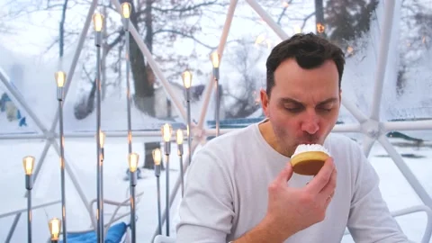 A man in a white sweater sits in the cafe and eats a cake with whipped cream Video stock 169965688