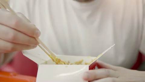 A man in a white t-shirt eats udon noodles with chicken, vegetables and spicy Stock Footage 135421188