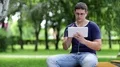 Man with white tablet computer sits on the bench in city park HD Footage