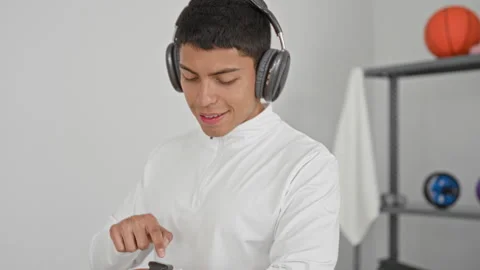 Man in white training top wearing headphones taps smartwatch in studio with.. Stock Footage 339251948