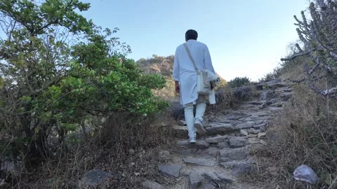 A man in white walks up a steep mountain path Vídeos de archivo 330333142