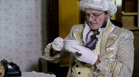 Man with a white wig is drinking a cup of tea Stock Footage 33035138