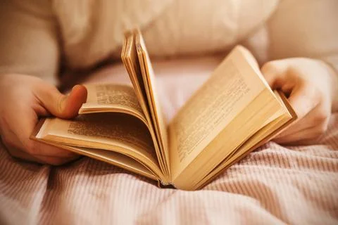 A man in a white wool sweater is lying on the bed and flipping through an old Stock Photos
