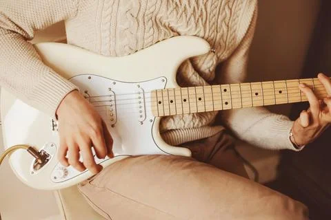 A man in a white wool sweater skillfully plays a melody on a white electric g Stock Photos