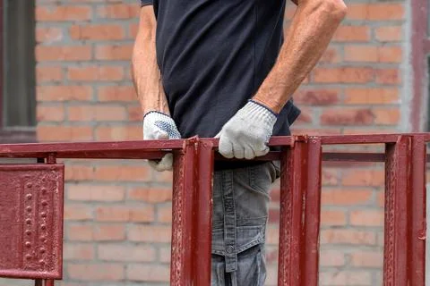 A man in white work gloves carries an iron ladder.Construction and repair wor Stock Photos