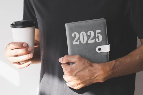 A man whose face is not visible hand holding grey diary with the text 2025 .. Stock Photos