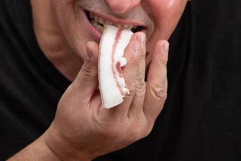 A man, whose face is not visible, eats a piece of lard. Stock Photos