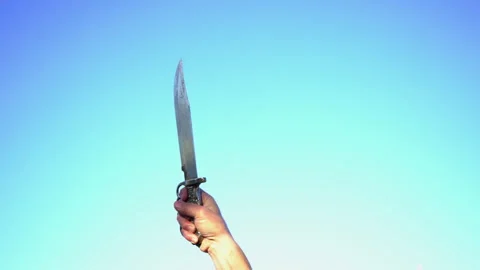A man wielding a large knife against a blue sky Stock Footage 256173868