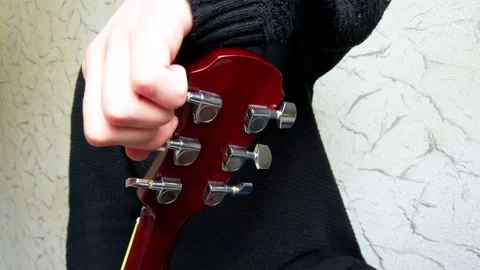 The man will tune the guitar. A man pulls the strings on a guitar. Stock Footage 147149638