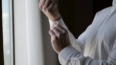 The man at the window is buttoning up the cuffs of a white shirt. Stock Footage 302284982