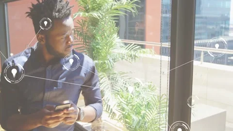 Man at window tapping phone, visualizing tech ideas as lightbulb network Stock Footage 332405912