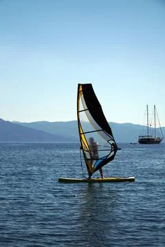 A man on a windsurf in the bay with a yacht in the background. Stock Photos