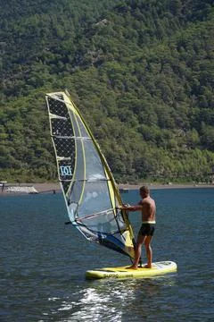 Man on a windsurf in the sea. Man learning to windsurf in the bay. Windsurfing. Stock Photos