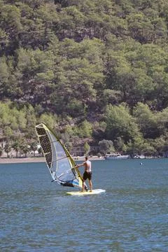 Man on a windsurf in the sea. Man learning to windsurf in the bay. Windsurfing. Stock Photos