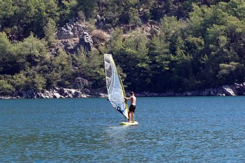 Man on a windsurf in the sea. Man learning to windsurf in the bay. Windsurfing. Stock Photos