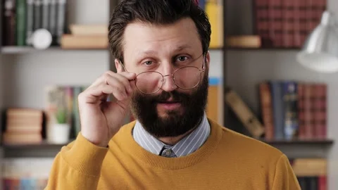 Man winks. Positive smiling bearded man with glasses in office or apartment room Vídeo Stock 147639584