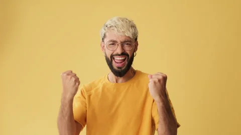 Man wins, waves hands triumphantly, looking at camera isolated on yellow Stock Footage 253934193