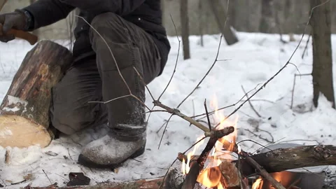 Man in winter clothes chopping trees and branches into fire on halt in hike Stock Footage 88370073