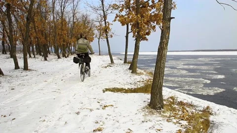 Man in winter clothes riding a bicycle in the snow Stock Footage 100452883