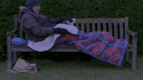 Man in winter clothing getting into sleeping bag on park bench at twilight. Stock Footage 155536705