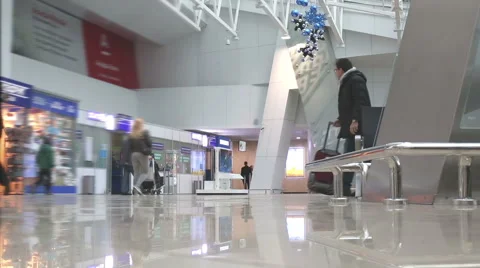 Man in winter coat with suitcase walking across waiting hall in the airport.  Vídeo Stock 64258260