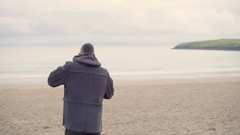 Man in winter coat walking on beach on cold day Stock Footage 113301625