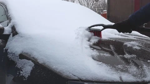 A man on a winter day cleans a brown car from snow with a special brush Vídeos de archivo 190442611
