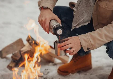 A man in the winter forest by the fire pours coffee Stock Photos