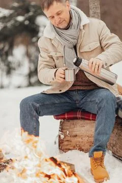 A man in the winter forest by the fire pours coffee Stock Photos