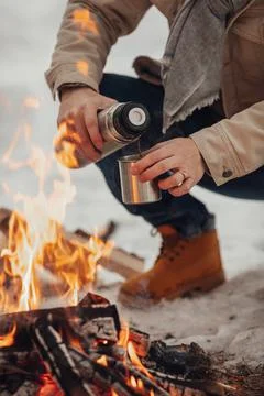 A man in the winter forest by the fire pours coffee Foto stock
