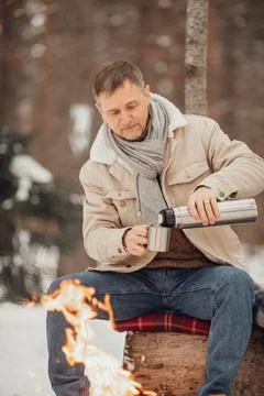 A man in the winter forest by the fire pours coffee Stock Photos