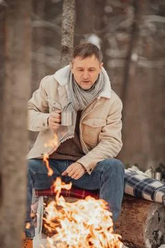 A man in the winter forest by the fire pours coffee Foto stock
