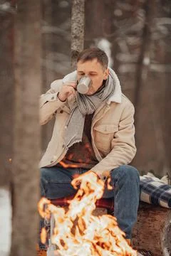A man in the winter forest by the fire pours coffee Foto stock