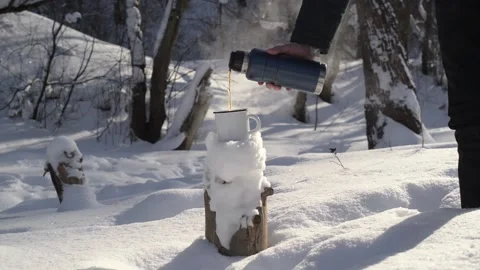 Man in winter forest pours hot tea from thermos into iron mug 库存影片 164093601