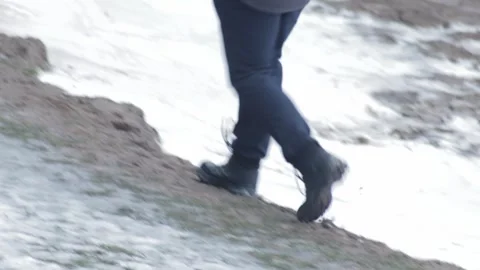 A man in winter shoes walks through melted snow, mud and puddles in spring. Stock-Footage 253472186