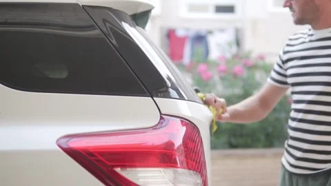 A man wipes dirt from dirt on the back of the car with a damp cloth. Stock Footage 252613775