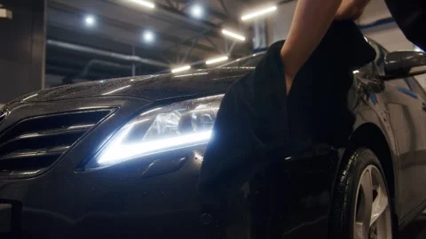 A man wipes the led headlight of a black car with his hands and a large towel Stock Footage 316415811