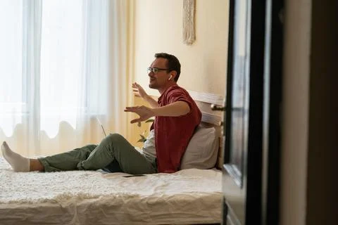 Man in wireless earbuds sitting on bed with laptop listening favorite music Stock-Fotos