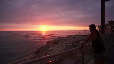 A man wistfully watching a beautiful sunset from the terrace of a beach house Stock Footage 194502811