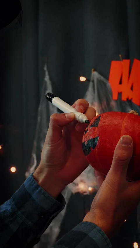 Man in witch hat paints scary face on pumpkin for Halloween. Vertical video Stock Footage 317198489